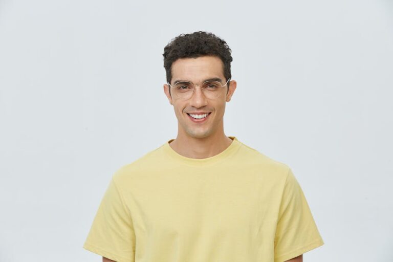 Portrait of a young man wearing glasses and a yellow shirt, smiling brightly.