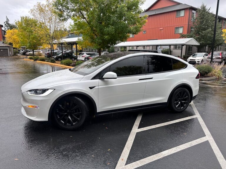 A sleek white electric SUV with tinted windows is parked in a Seattle neighborhood on a rainy fall day.